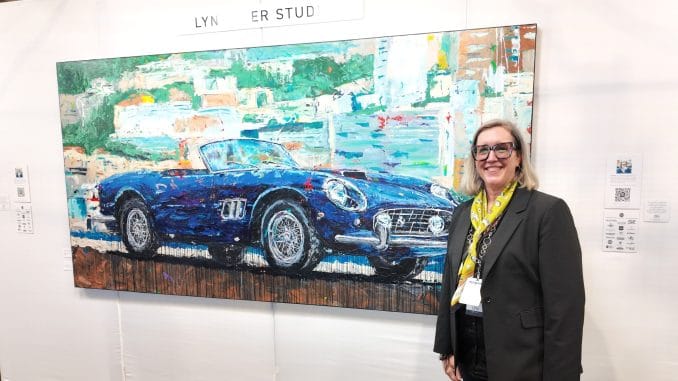 When the Microphone Died, the Real Interview Began — Lyn Hiner at Pebble Beach Automotive artist Lyn Hiner smiling beside her hand-painted blue Ferrari 250 GT SWB California Spyder artwork at the RetroAuto Pavilion, Pebble Beach Concours d'Elegance 2026